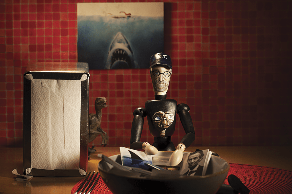 Aprenda a ser criativo Boneco de Steven Spielberg com elementos à volta sobre seus filmes (Tubarão, Lincoln, Jurassic Park)